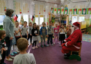 Dzieci stoją w półkolu i śpiewając Mikołajowi piosenkę.